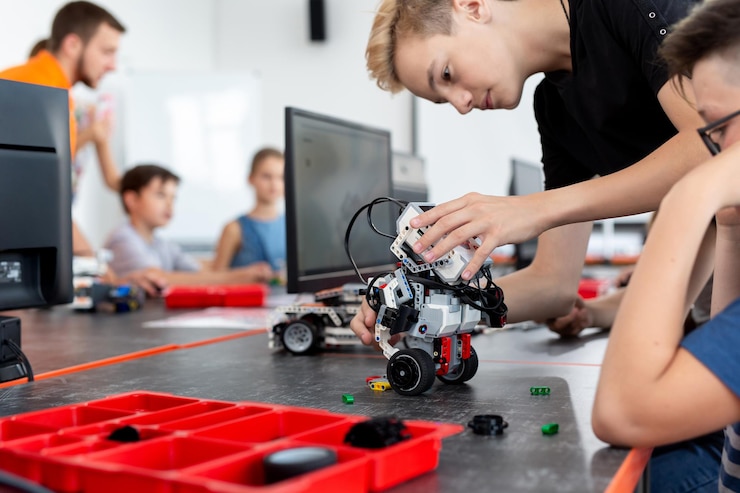 Foto colegial inteligente sentado en la mesa y construyendo un dispositivo robótico en una lección escolar