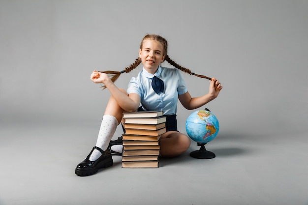 Colegial isolada em fundo amarelo com globo. menina com uniforme escolar, sentada sobre um fundo amarelo, lendo um livro. menina loira com uniforme escolar em um fundo amarelo