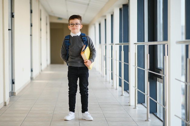 Colegial con mochila y libros en la escuela Concepto de educación Regreso a la escuela Colegial yendo a clase Chico elegante con mochila Chico listo para estudiar