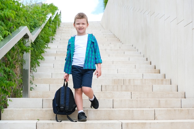 El colegial con una mochila en la mano en la calle de camino a la escuela baja las escaleras. De vuelta a la escuela.