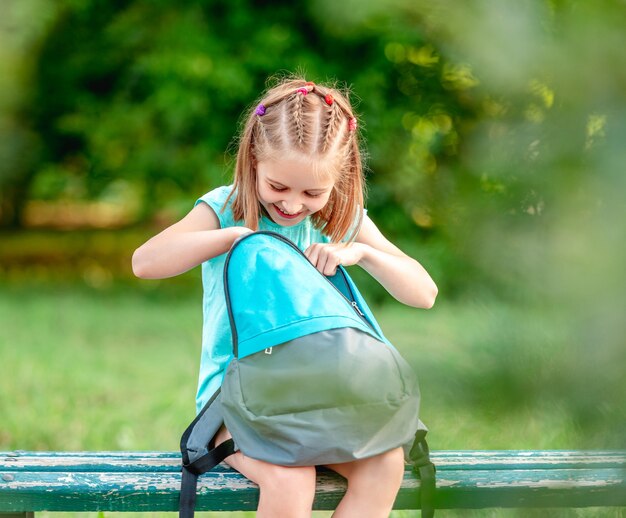 Colegial olhando para a mochila aberta no banco do parque