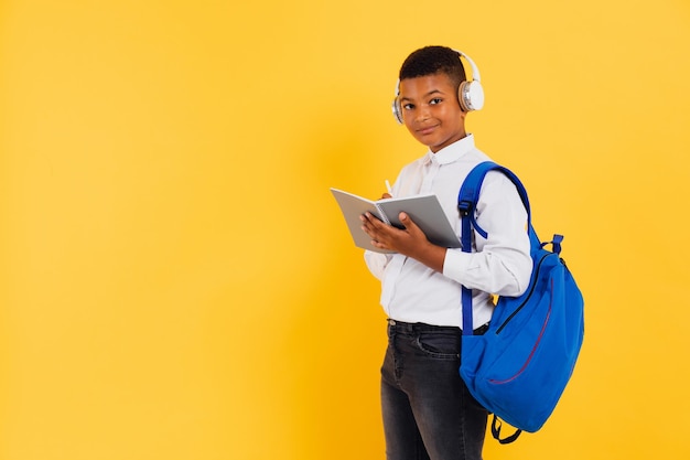 Colegial de raza mixta feliz con auriculares y mochila con libros y cuadernos Concepto de regreso a la escuela