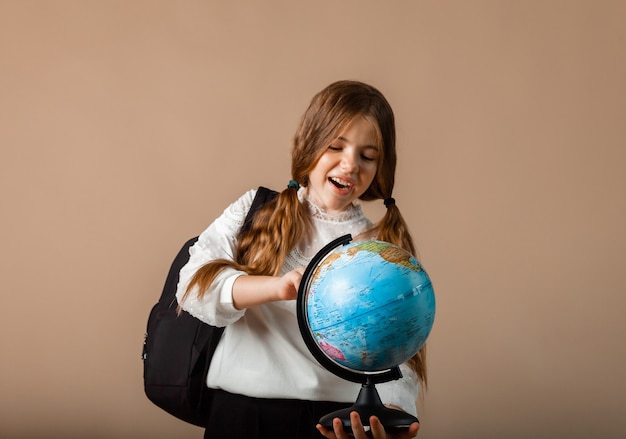 Colegial segurando o globo, mostrando com o dedo o espaço em branco, isolado no fundo do estúdio