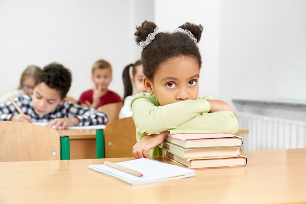 Colegial, sentado à mesa na sala de aula, apoiando-se nos livros.