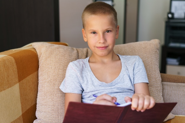 de colegial sentado en el sofá haciendo la tarea niño feliz niño sosteniendo la pluma para escribir niño