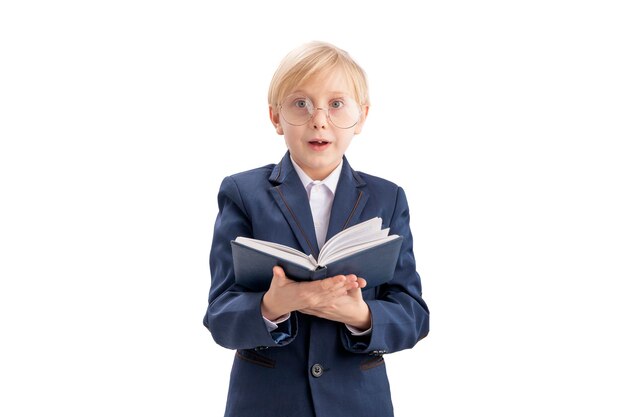 Colegial sorprendido con gafas grandes y libro en las manos Niño rubio en uniforme escolar lee libros de texto Aislado sobre fondo blanco