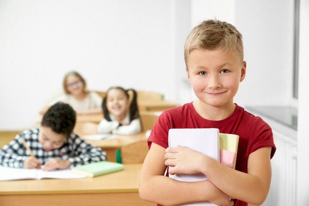 Colegial sosteniendo libros, mirando a cámara, sonriendo.