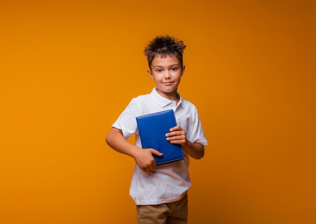 Un colegial sostiene un libro azul sobre un fondo amarillo de regreso a la escuela