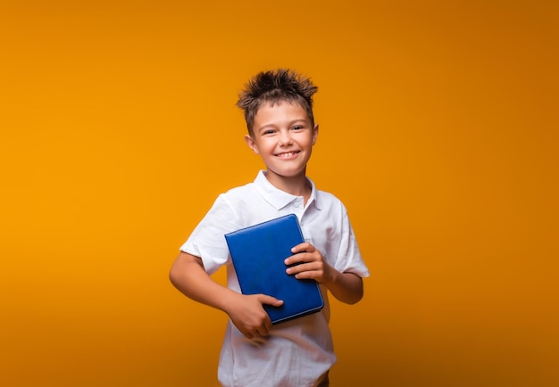 Foto un colegial sostiene un libro azul sobre un fondo amarillo de regreso a la escuela