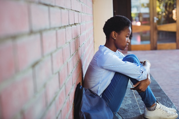 Colegial triste sentada contra uma parede de tijolos