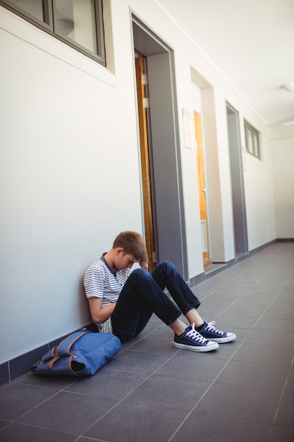 Colegial triste sentado en el pasillo