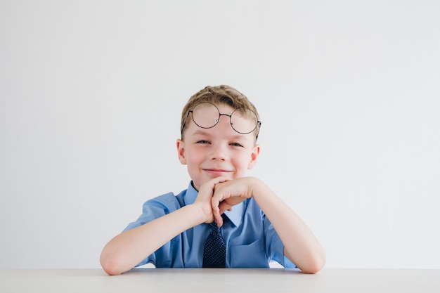 Colegial en uniforme escolar y gafas sentado en el escritorio