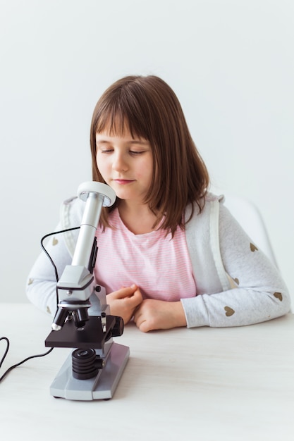 Colegial usando microscópio na aula de Ciências. Conceito de tecnologias, lições e crianças.