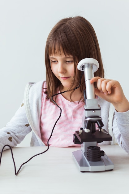 Colegial usando microscópio na aula de Ciências. Conceito de tecnologias, lições e crianças.