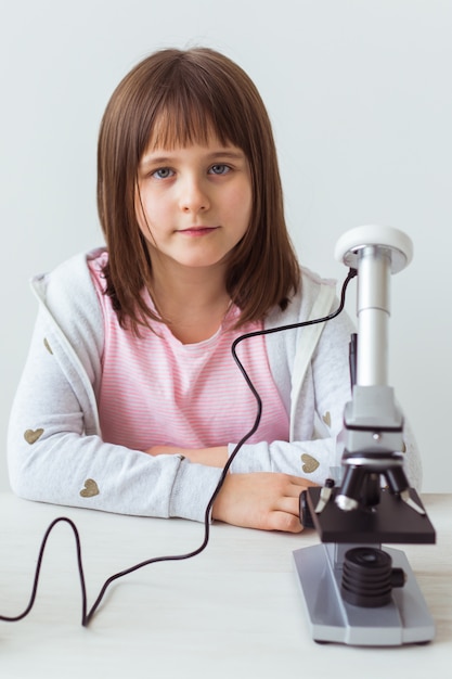 Colegial usando microscópio na aula de Ciências. Conceito de tecnologias, lições e crianças.