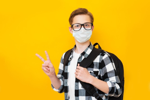 El colegial vistiendo mascarilla médica con una mochila sobre un fondo amarillo aislado