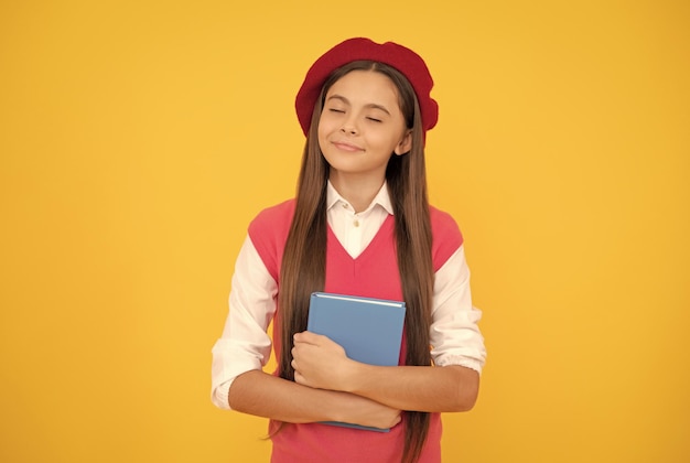 Una colegiala adolescente de ensueño con boina francesa sostiene un cuaderno sobre un sueño de fondo amarillo