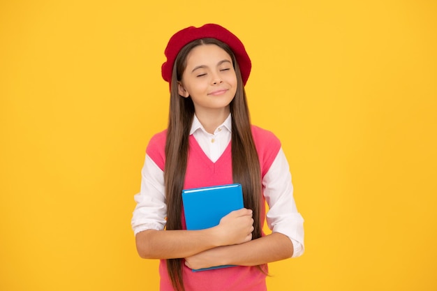 Una colegiala adolescente de ensueño con boina francesa sostiene un cuaderno sobre un sueño de fondo amarillo