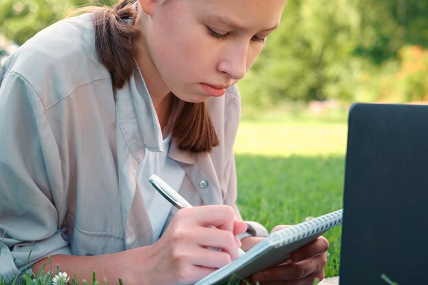 Colegiala adolescente estudiando leyendo sus libros, tableta y portátil sentada al aire libre Regreso a la escuela Chica estudiante tumbada en la hierba verde usando una computadora portátil en el patio de la universidad o en el parque Aprendizaje a distancia