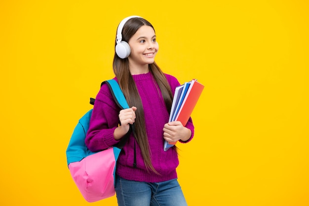 Colegiala adolescente estudiante chica en auriculares mantenga libros sobre fondo amarillo estudio aislado