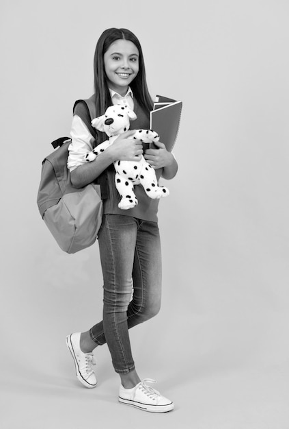 Colegiala adolescente feliz con mochila y cuaderno sostiene juguete en la lección de fondo amarillo