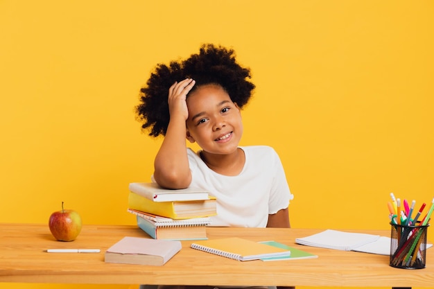 Colegiala afroamericana feliz haciendo la tarea mientras está sentada en el escritorio Concepto de regreso a la escuela