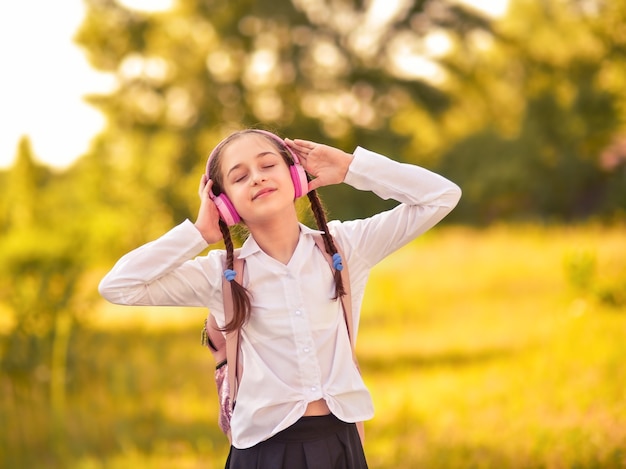 Colegiala al aire libre. Hermosa niña escuchando música con auriculares en el parque otoño