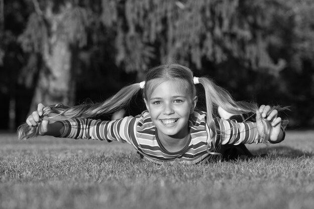 Colegiala alegre en un día soleado Alumno sonriente feliz Diviértete Niña niño tendido hierba verde Niño feliz emocional saludable relajarse al aire libre Peinado de cola de caballo niña disfrutar relajarse Vivir una vida feliz