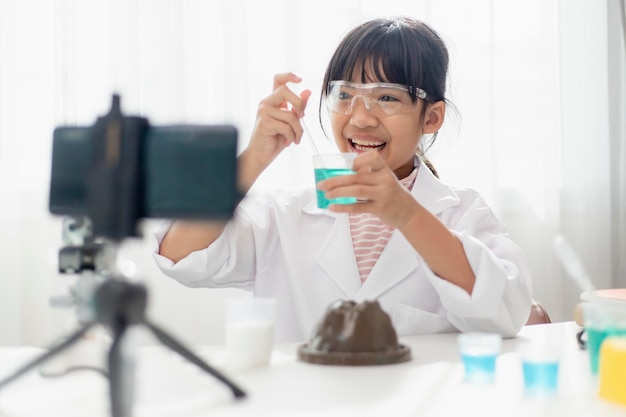 Colegiala asiática haciendo experimentos de química fáciles y grabando un video para sus seguidores Joven bloguero posando frente a la cámara para vlog Los niños hacen vlog para el concepto de canal de redes sociales