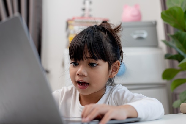 Colegiala asiática haciendo su tarea con una computadora portátil en casa Los niños usan aparatos para estudiar Educación y aprendizaje a distancia para niños Educación en el hogar durante la cuarentena Quédese en casa