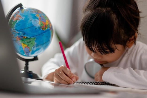 Colegiala asiática haciendo su tarea con una computadora portátil en casa Los niños usan aparatos para estudiar Educación y aprendizaje a distancia para niños Educación en el hogar durante la cuarentena Quédese en casa