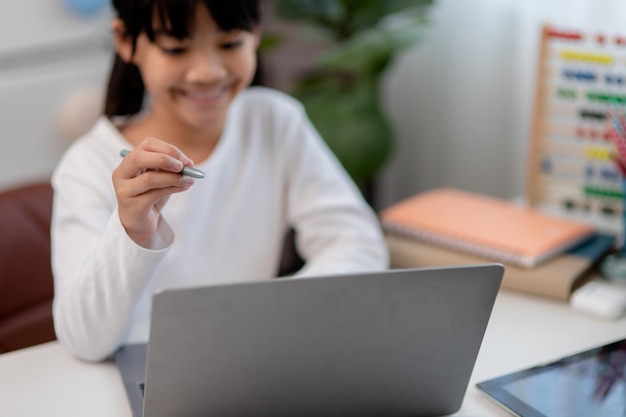 Colegiala asiática haciendo su tarea con una computadora portátil en casa Los niños usan aparatos para estudiar Educación y aprendizaje a distancia para niños Educación en el hogar durante la cuarentena Quédese en casa