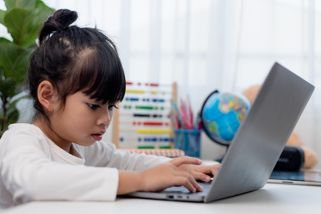 Colegiala asiática haciendo su tarea con una computadora portátil en casa Los niños usan aparatos para estudiar Educación y aprendizaje a distancia para niños Educación en el hogar durante la cuarentena Quédese en casa