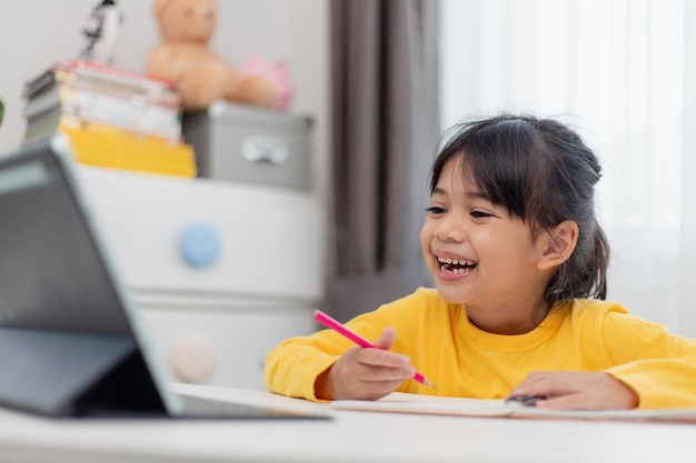 Colegiala asiática haciendo su tarea con tableta digital en casa Los niños usan aparatos para estudiar Educación y aprendizaje a distancia para niños Educación en el hogar durante la cuarentena Quédate en casa