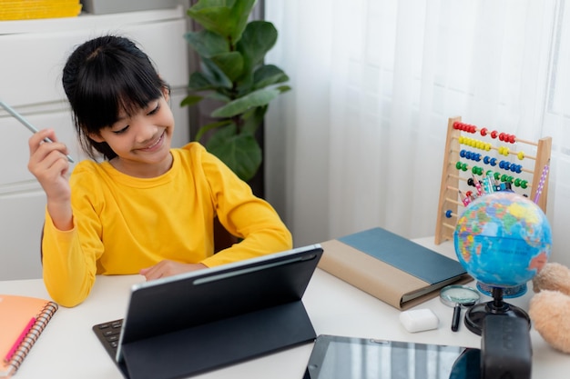 Colegiala asiática haciendo su tarea con tableta digital en casa Los niños usan aparatos para estudiar Educación y aprendizaje a distancia para niños Educación en el hogar durante la cuarentena Quédate en casa