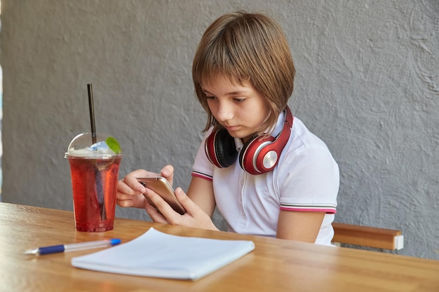 Colegiala con auriculares y limonada tiene teléfono inteligente en manos niña usando teléfono móvil