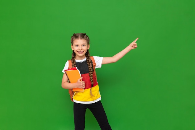 Una colegiala con una bandera alemana en su camiseta señala hacia un lado un anuncio sobre un fondo verde aislado Educación en el extranjero