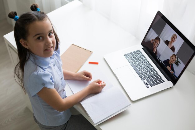 Foto colegiala bastante elegante que estudia matemáticas de tarea durante su lección en línea en casa, distancia social durante la cuarentena, autoaislamiento, concepto de educación en línea, educador en casa