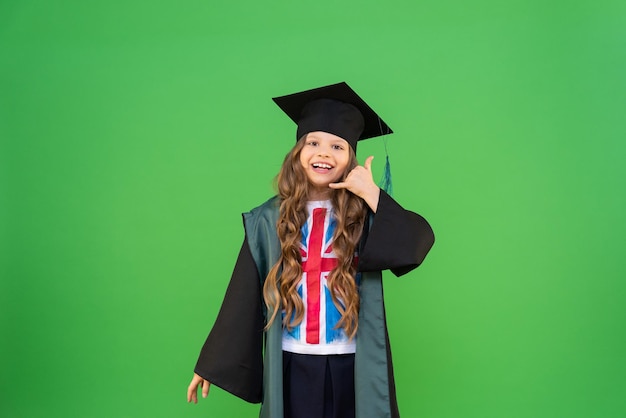 Una colegiala con bata de graduada y gorra de maestro hace un gesto con la mano de que está llamando por teléfono cursos de inglés