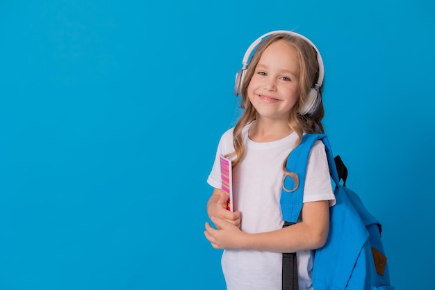 colegiala con una camiseta blanca, auriculares, una mochila en el hombro y un cuaderno a rayas