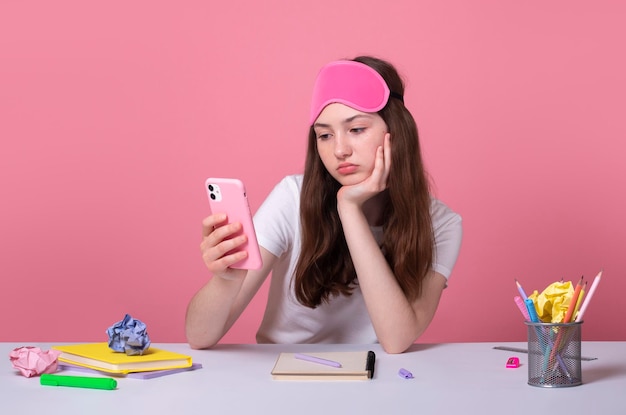 Una colegiala cansada y perezosa aburrida sostiene un teléfono celular inteligente en la mano y mira la pantalla