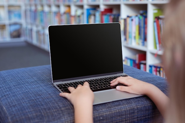 Colegiala caucásica en el escritorio de la biblioteca escolar usando una computadora portátil, con espacio de copia en la pantalla