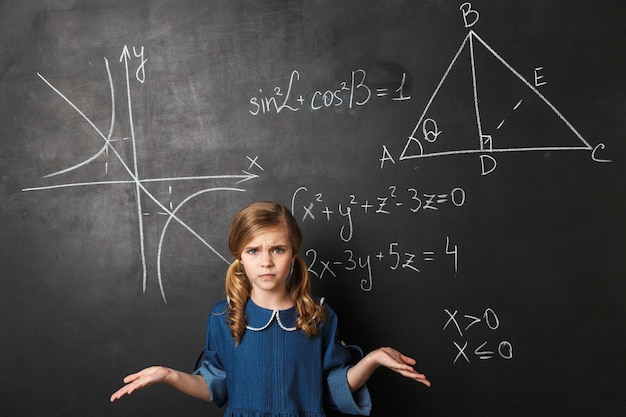 Colegiala confusa de pie en la pizarra con gráficos matemáticos escritos en él