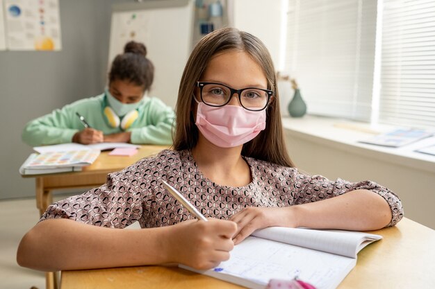 Colegiala contemporánea en máscara y anteojos mirándote