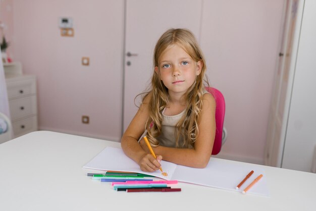 Colegiala con un dibujo pensativo en un cuaderno con la mano derecha o hace la tarea y mira a la cámara