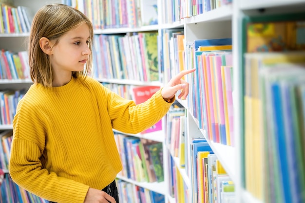 Colegiala eligiendo libro en la biblioteca escolar