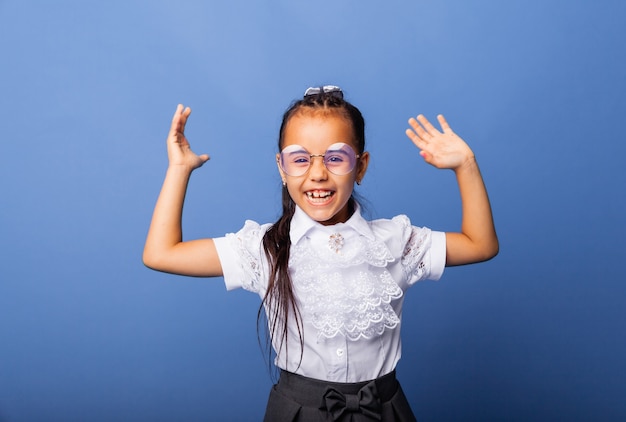 Colegiala emocionada y sorprendida sonriendo con las manos levantadas sobre fondo azul aislado color de fondo amarillo