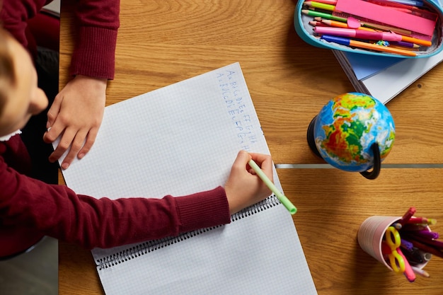 Colegiala enfocada sentada en el escritorio haciendo la tarea de escritura a mano educación en el hogar