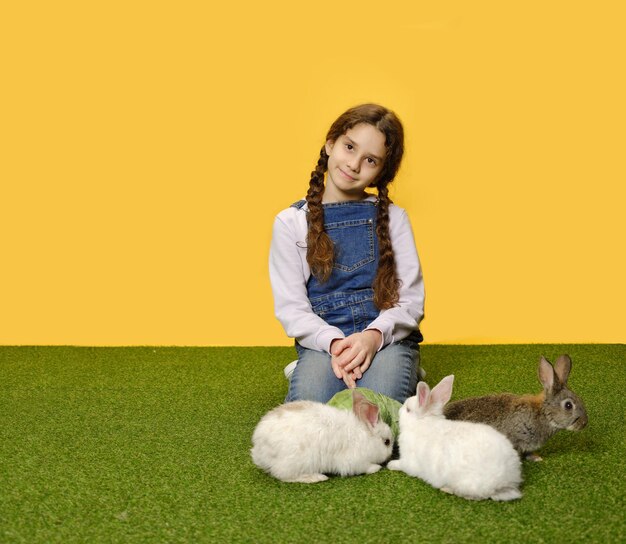 La colegiala está acostada jugando con los conejitos en el fondo amarillo del estudio Copiar espacio