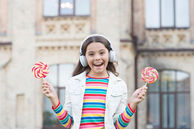 Colegiala de estilo de vida saludable con piruleta niño feliz en auriculares alumno escuchar música y cantar canciones regreso a la escuela belleza feliz niño al aire libre educación innovadora feliz día de los niños Felicidad